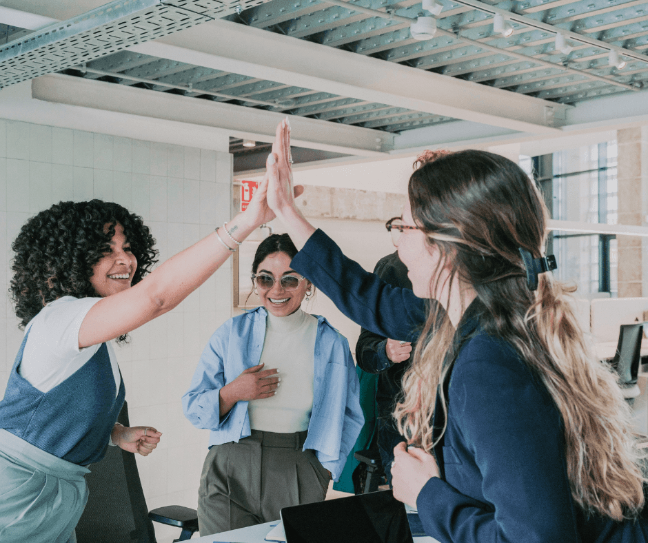 Group of colleagues giving high fives in an office setting with desks and chairs in the background.